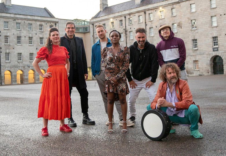 A group of seven people standing and kneeling in a plaza one of them holds a bodhran
