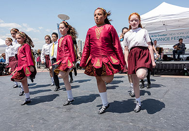 A group of children in Irish dance costumes, dancing outside.